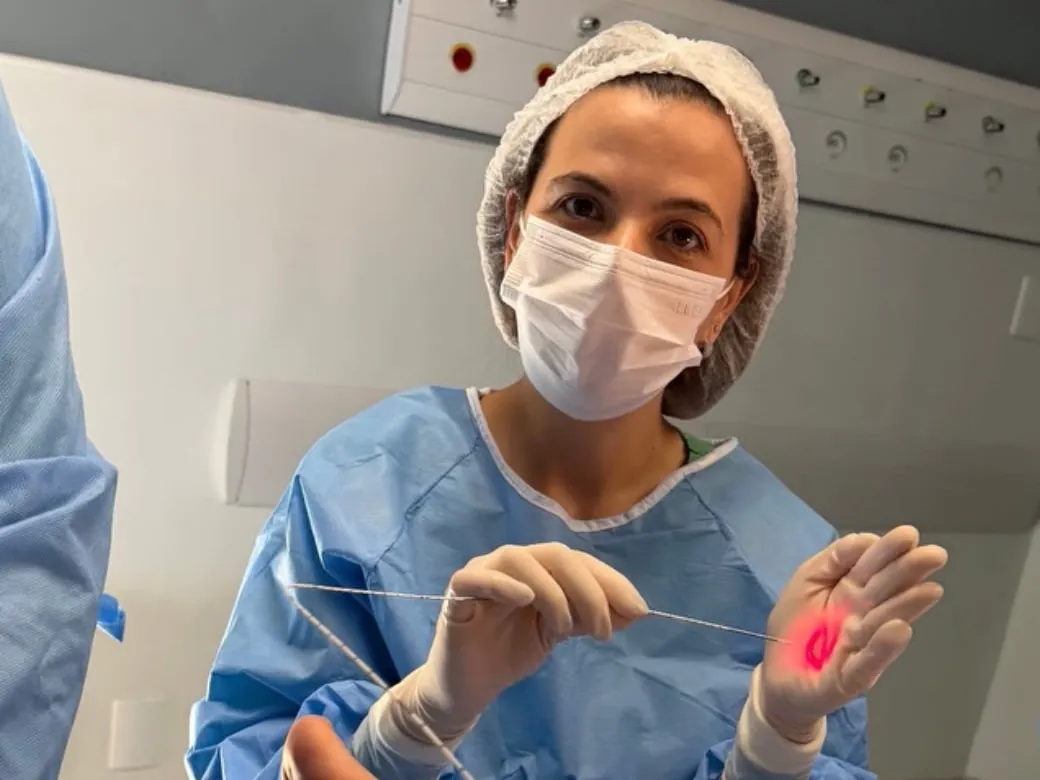 Dra. Lais Rizzato Rezende segurando a fibra do endolaser, com a luz de guia acesa, em ambiente hospitalar